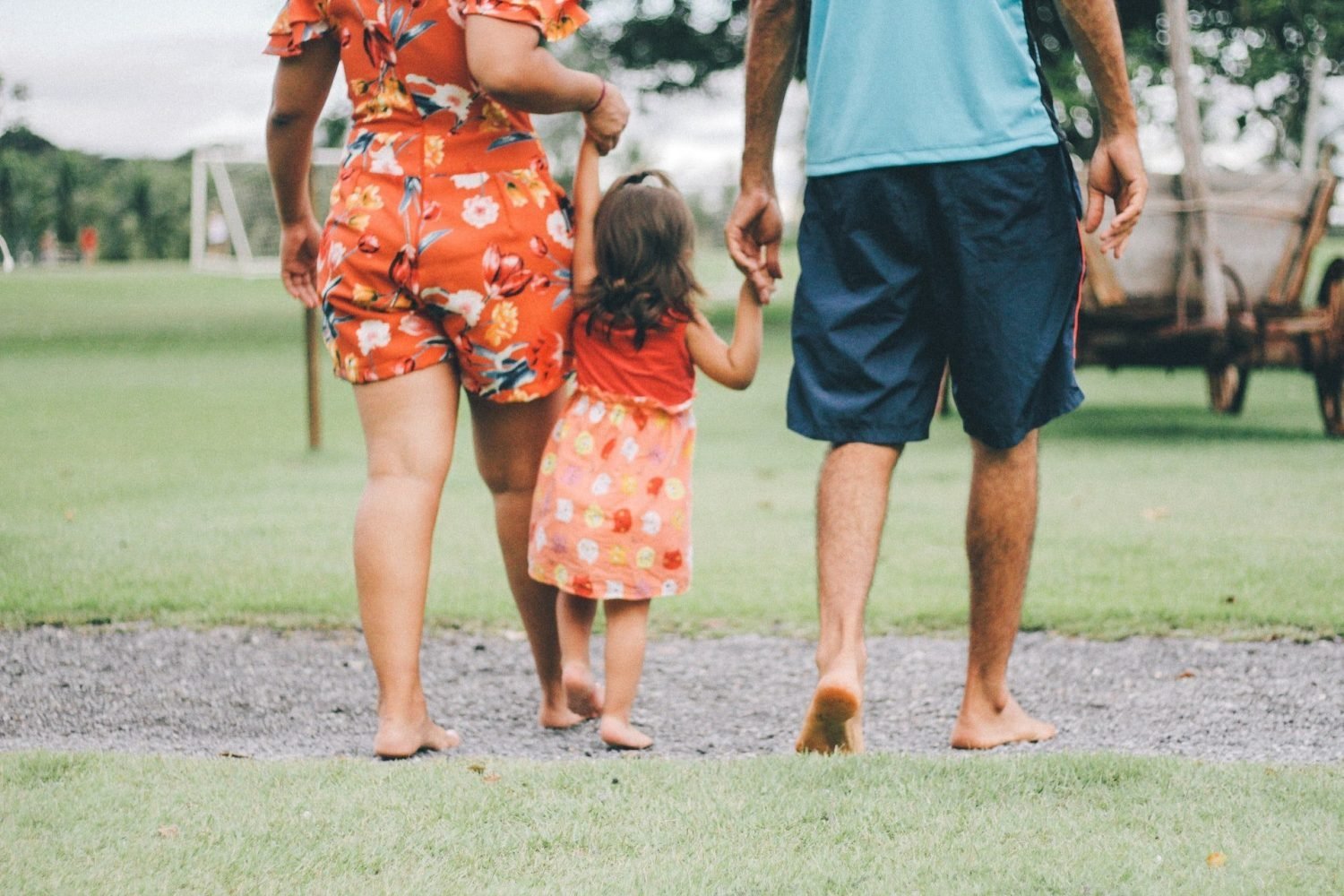 Mother and father holding hands with a little girl while walking in a park